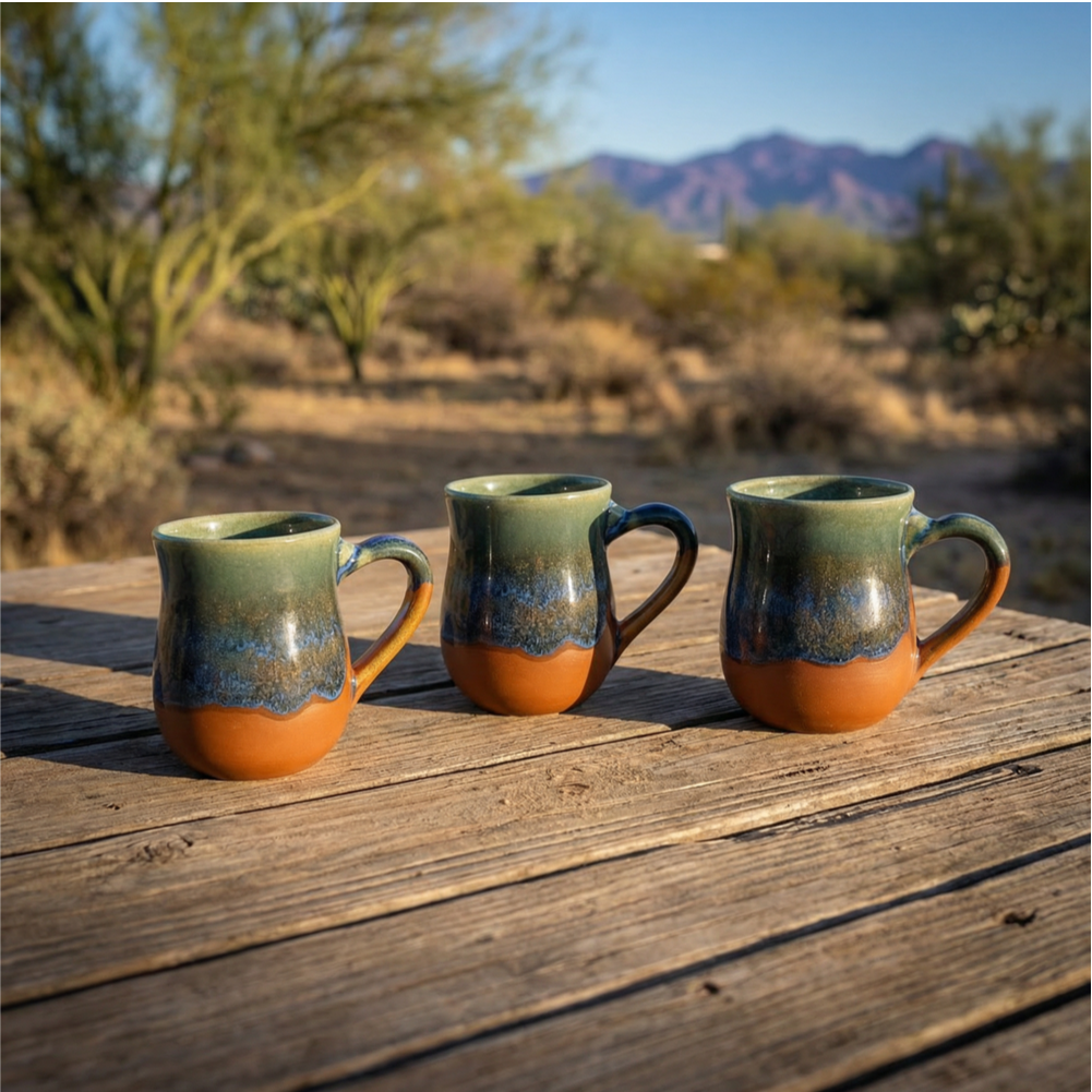 Three HF Coors Blue Bayou reactive glaze 15oz mugs on a weathered wood table in the Sonoran desert with palo verde trees and mountains in Tucson Arizona handcrafted American-made ceramic